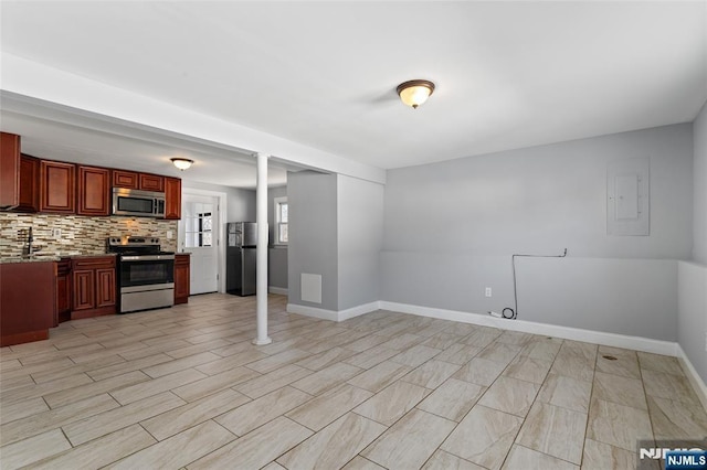 kitchen with light stone counters, baseboards, electric panel, appliances with stainless steel finishes, and backsplash