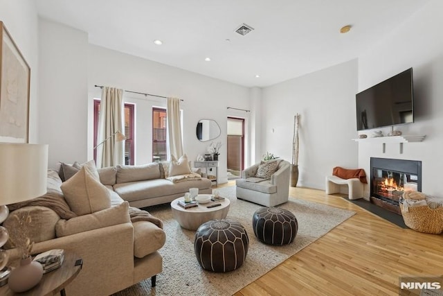 living area featuring a glass covered fireplace, recessed lighting, wood finished floors, and visible vents