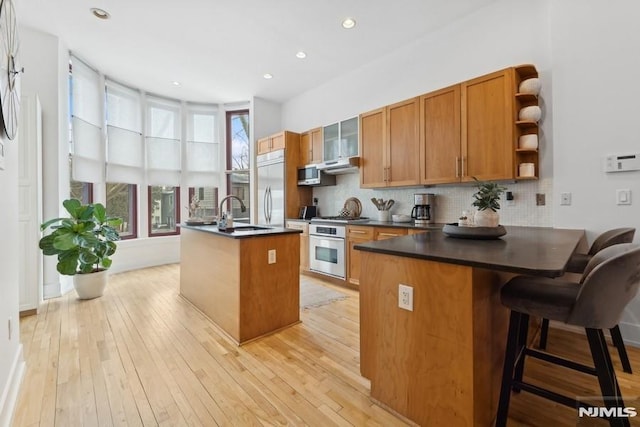 kitchen with open shelves, tasteful backsplash, dark countertops, stainless steel appliances, and brown cabinetry