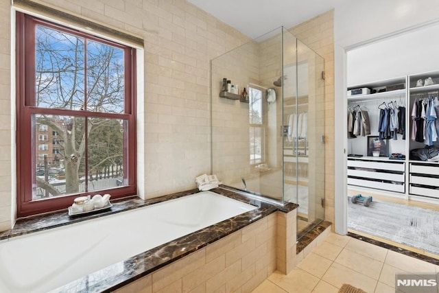 bathroom featuring tile patterned floors, a spacious closet, a bath, and a shower stall