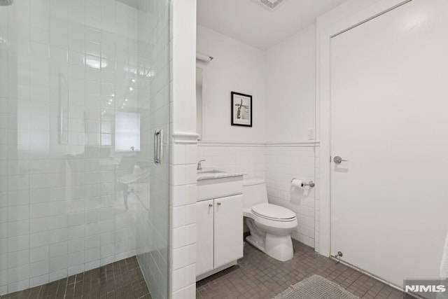 bathroom with tile patterned floors, toilet, a tile shower, tile walls, and vanity