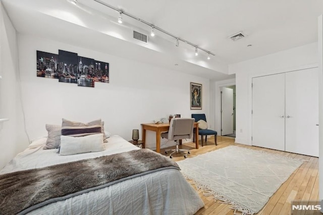 bedroom with wood finished floors, visible vents, and a closet