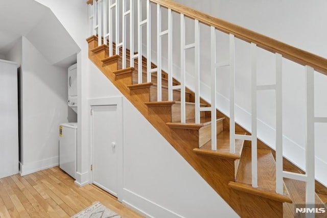 staircase with stacked washer and clothes dryer and wood finished floors