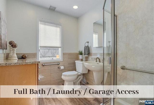 full bathroom featuring tile walls, toilet, visible vents, and wainscoting