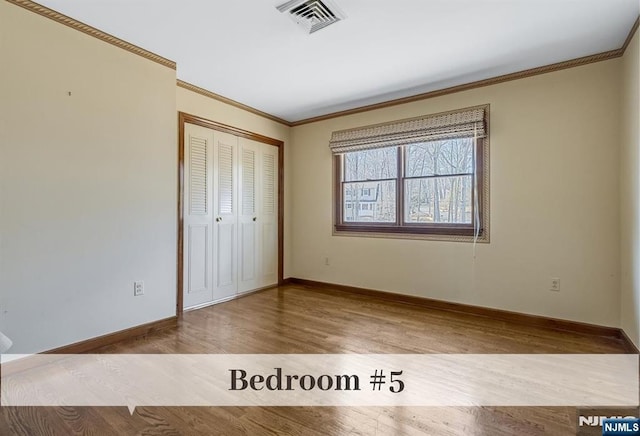 unfurnished bedroom with visible vents, crown molding, baseboards, wood finished floors, and a closet