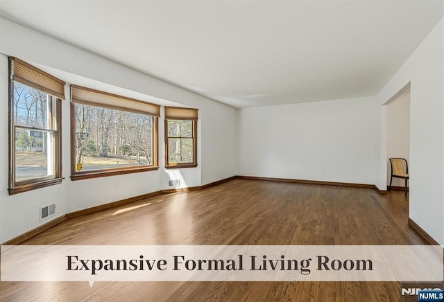 unfurnished room with a wealth of natural light, visible vents, baseboards, and wood finished floors