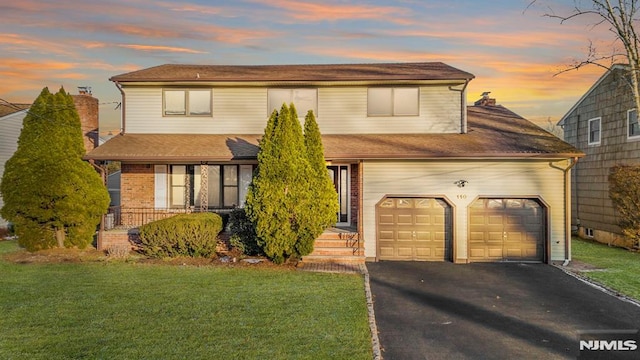 traditional home featuring aphalt driveway, an attached garage, a lawn, and brick siding