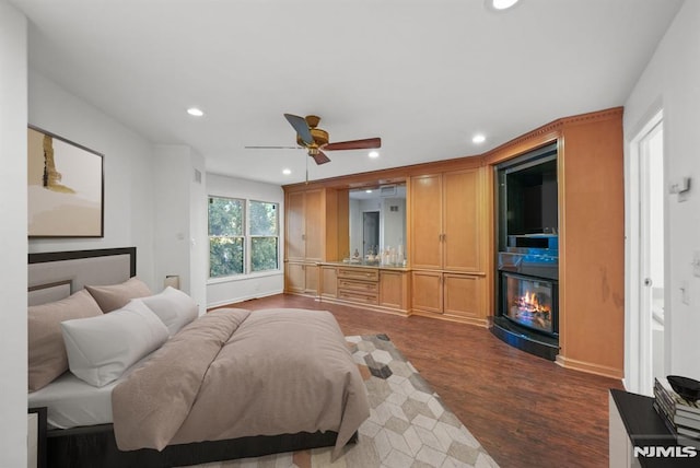 bedroom with recessed lighting, dark wood-type flooring, a glass covered fireplace, and a ceiling fan