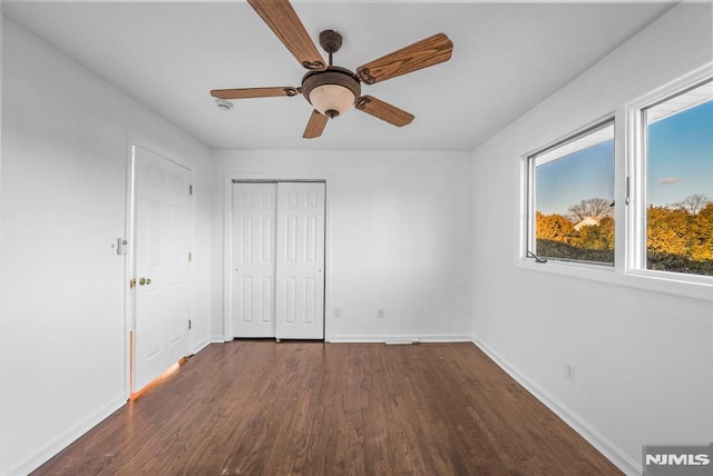 unfurnished bedroom featuring a closet, baseboards, dark wood-type flooring, and a ceiling fan