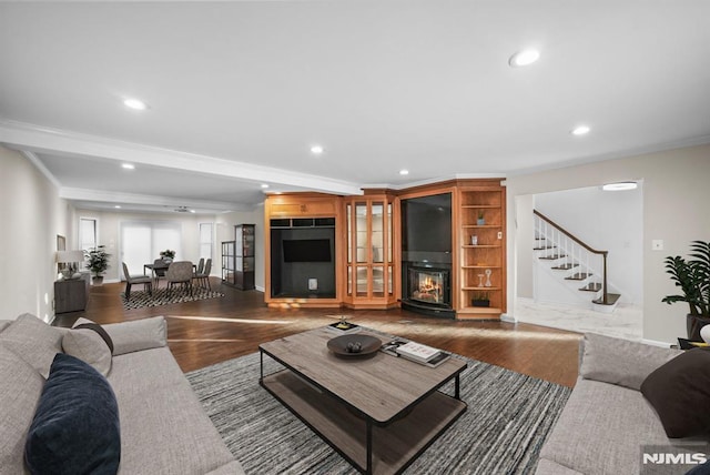 living area with wood finished floors, recessed lighting, ornamental molding, stairs, and a glass covered fireplace