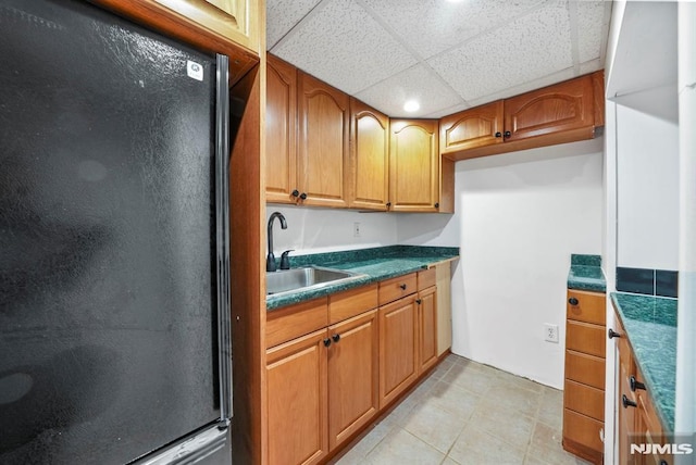 kitchen with freestanding refrigerator, a sink, a paneled ceiling, dark countertops, and brown cabinets