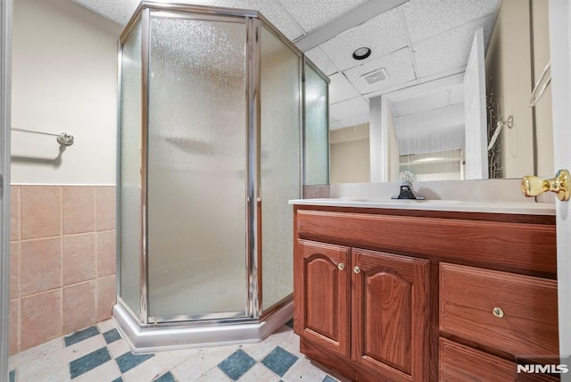 bathroom with vanity, a stall shower, a drop ceiling, tile patterned floors, and tile walls