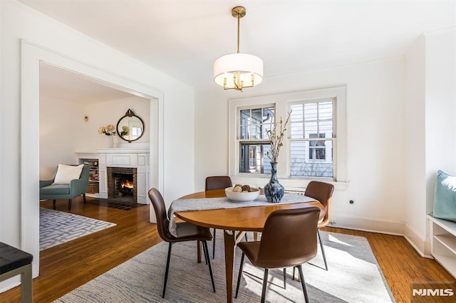 dining space with a fireplace with flush hearth, wood finished floors, baseboards, and a chandelier