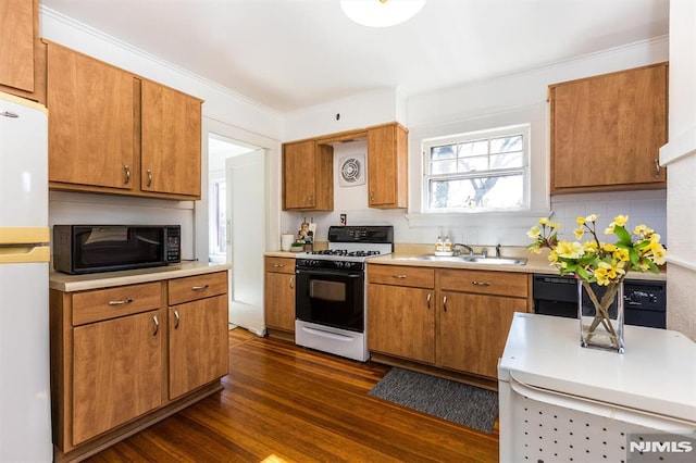 kitchen featuring black microwave, light countertops, freestanding refrigerator, gas stove, and a sink