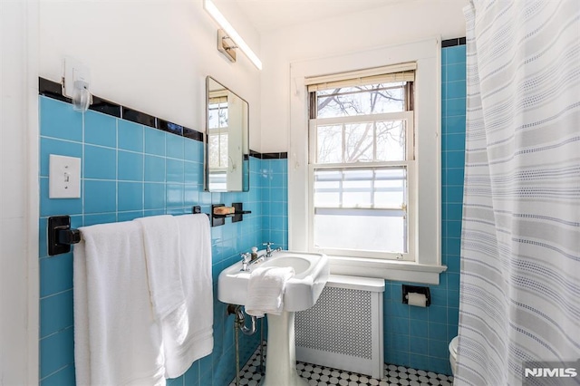 bathroom featuring a shower with curtain, tile walls, radiator heating unit, and a wainscoted wall