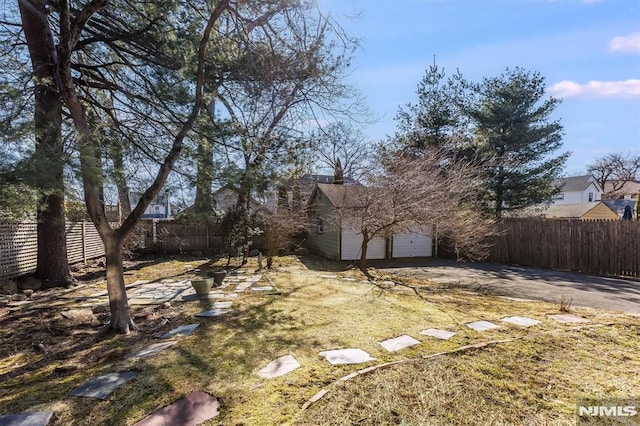 view of yard with an outdoor structure, an attached garage, fence private yard, and driveway