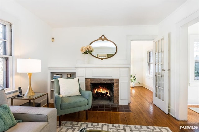 living room featuring a brick fireplace, baseboards, and wood finished floors