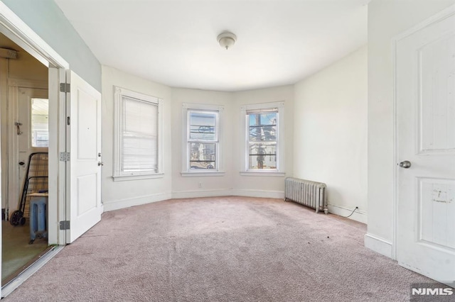 carpeted empty room featuring baseboards and radiator