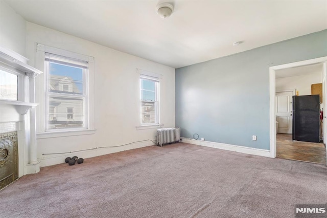 carpeted empty room with radiator, a fireplace, and baseboards