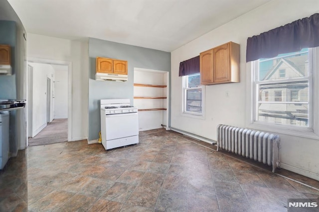 kitchen with under cabinet range hood, stone finish flooring, radiator, baseboards, and white range with gas stovetop