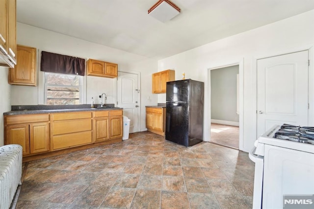 kitchen featuring a sink, dark countertops, radiator heating unit, freestanding refrigerator, and white range with gas stovetop