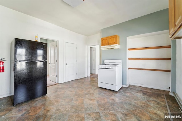 kitchen with baseboards, white range with gas stovetop, freestanding refrigerator, under cabinet range hood, and stone finish flooring