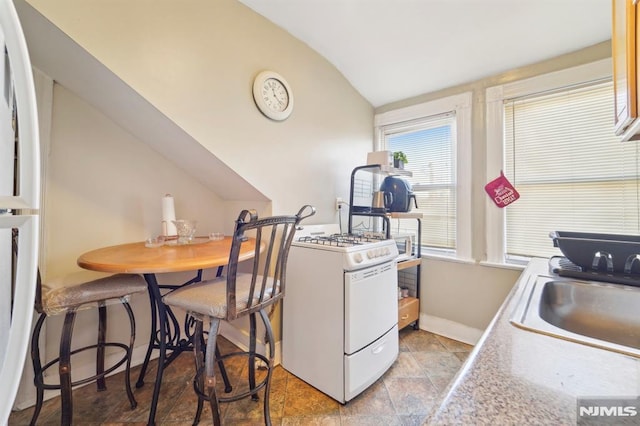 kitchen featuring a sink, white appliances, baseboards, and vaulted ceiling