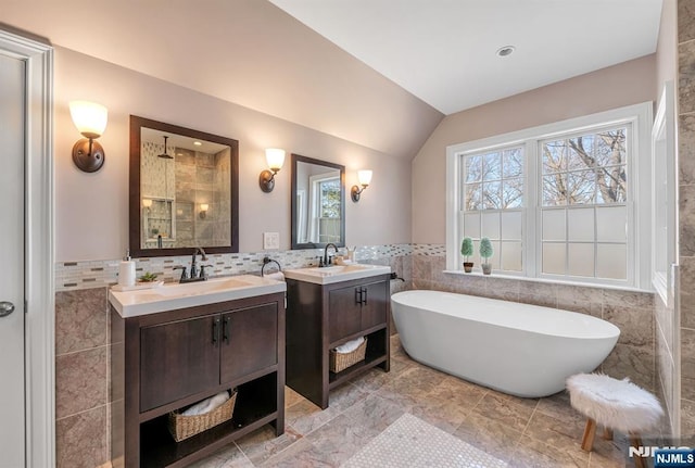 bathroom with a freestanding bath, tile walls, a wealth of natural light, and a sink