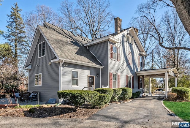 view of property exterior with a shingled roof, a patio, driveway, and a chimney