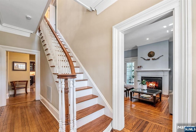 stairway featuring a glass covered fireplace, visible vents, wood-type flooring, and ornamental molding