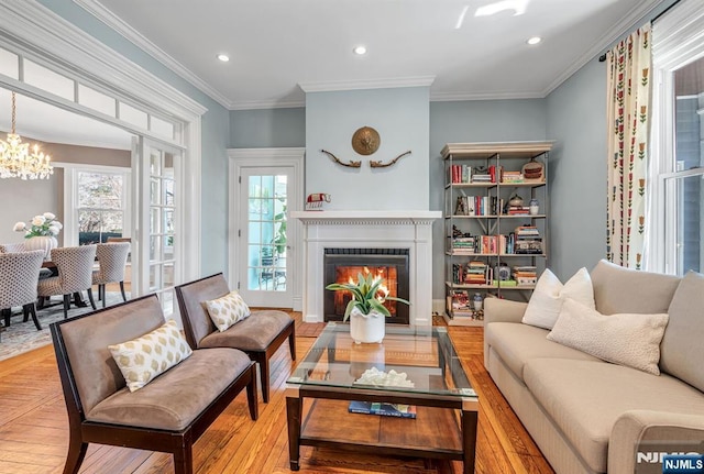 living area featuring recessed lighting, wood-type flooring, a lit fireplace, an inviting chandelier, and crown molding