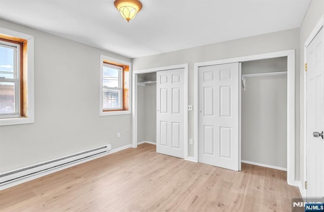 unfurnished bedroom featuring light wood-style floors, a baseboard heating unit, baseboards, and two closets