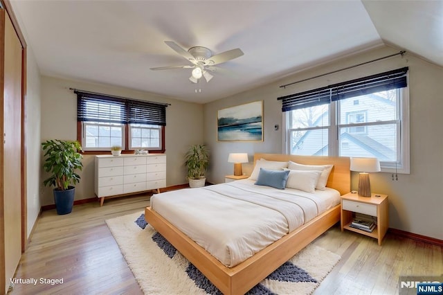 bedroom with lofted ceiling, multiple windows, baseboards, and light wood finished floors