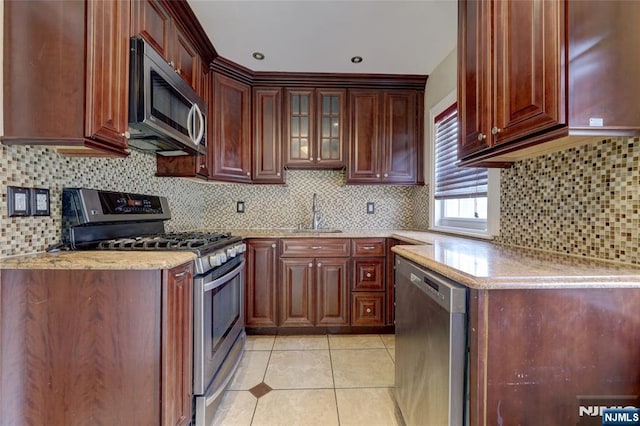 kitchen featuring light stone countertops, light tile patterned flooring, a sink, appliances with stainless steel finishes, and backsplash