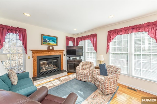 living room featuring baseboards, visible vents, light wood finished floors, recessed lighting, and a glass covered fireplace