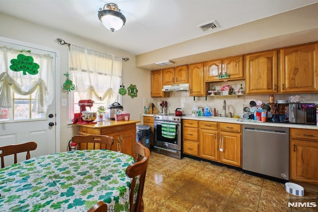 kitchen featuring a sink, light countertops, under cabinet range hood, appliances with stainless steel finishes, and brown cabinets