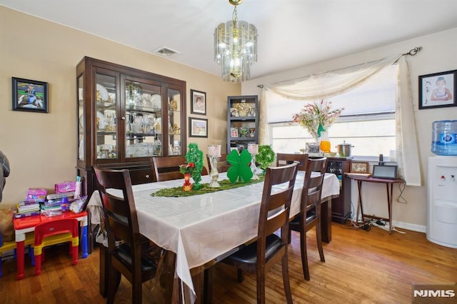 dining space featuring baseboards, wood finished floors, visible vents, and a chandelier