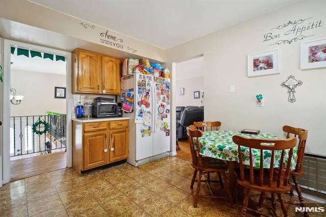 kitchen with brown cabinetry, a toaster, freestanding refrigerator, light countertops, and backsplash