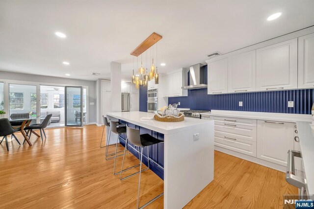 kitchen featuring white cabinetry, light countertops, light wood-style flooring, and wall chimney exhaust hood