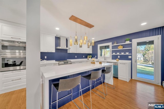 kitchen featuring wall chimney range hood, light countertops, a wealth of natural light, appliances with stainless steel finishes, and white cabinets