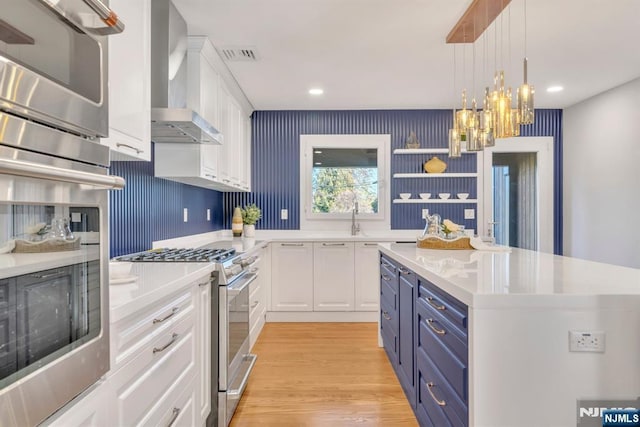 kitchen with visible vents, wall chimney range hood, appliances with stainless steel finishes, white cabinetry, and blue cabinets