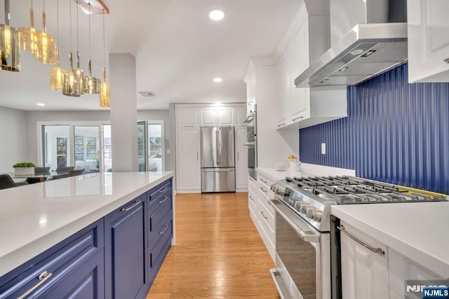 kitchen featuring white cabinets, stainless steel appliances, light countertops, and wall chimney range hood