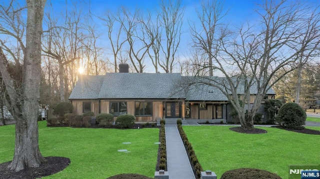 view of front facade featuring a chimney, a front lawn, and a shingled roof