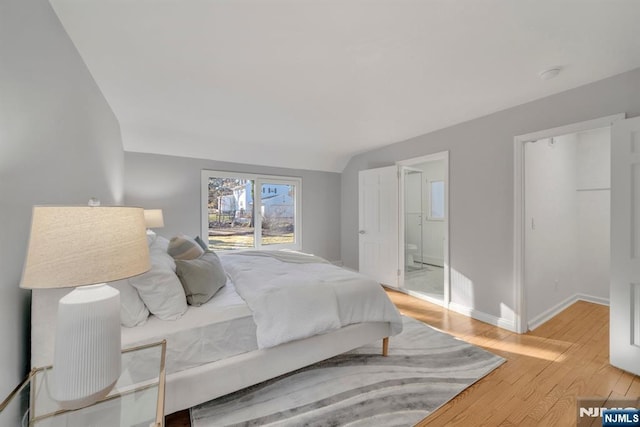 bedroom with baseboards, ensuite bathroom, and light wood finished floors