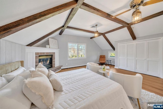 bedroom featuring visible vents, vaulted ceiling with beams, baseboard heating, a fireplace, and wood finished floors