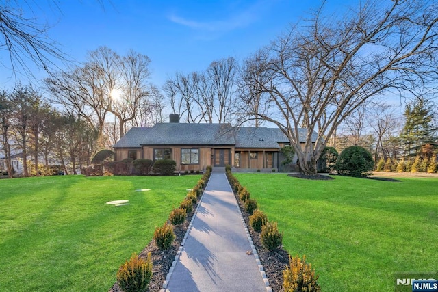 ranch-style home with driveway, a chimney, and a front lawn