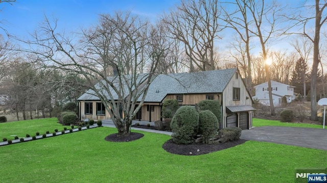 view of front facade featuring driveway, a shingled roof, a front lawn, a garage, and board and batten siding