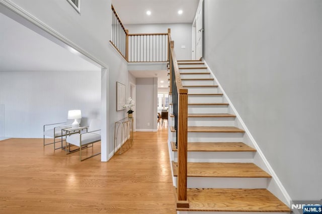 stairway with recessed lighting, baseboards, a high ceiling, and wood finished floors