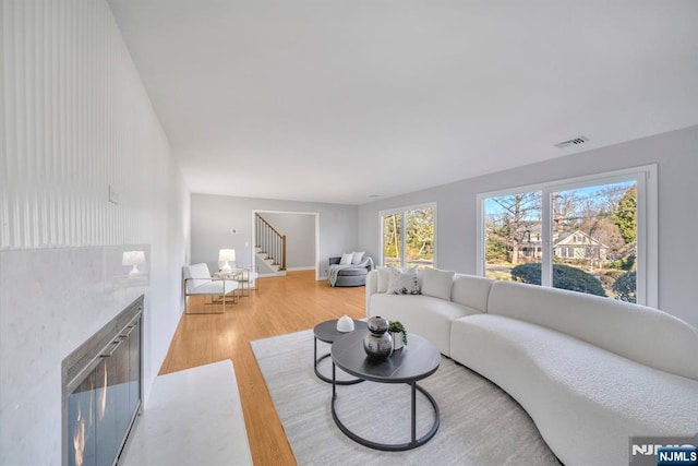 living room featuring visible vents, a glass covered fireplace, stairs, and light wood finished floors