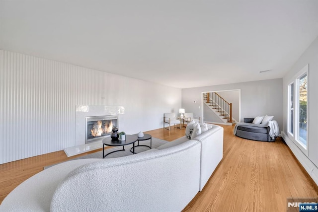 living room with stairway, light wood-style floors, and a glass covered fireplace